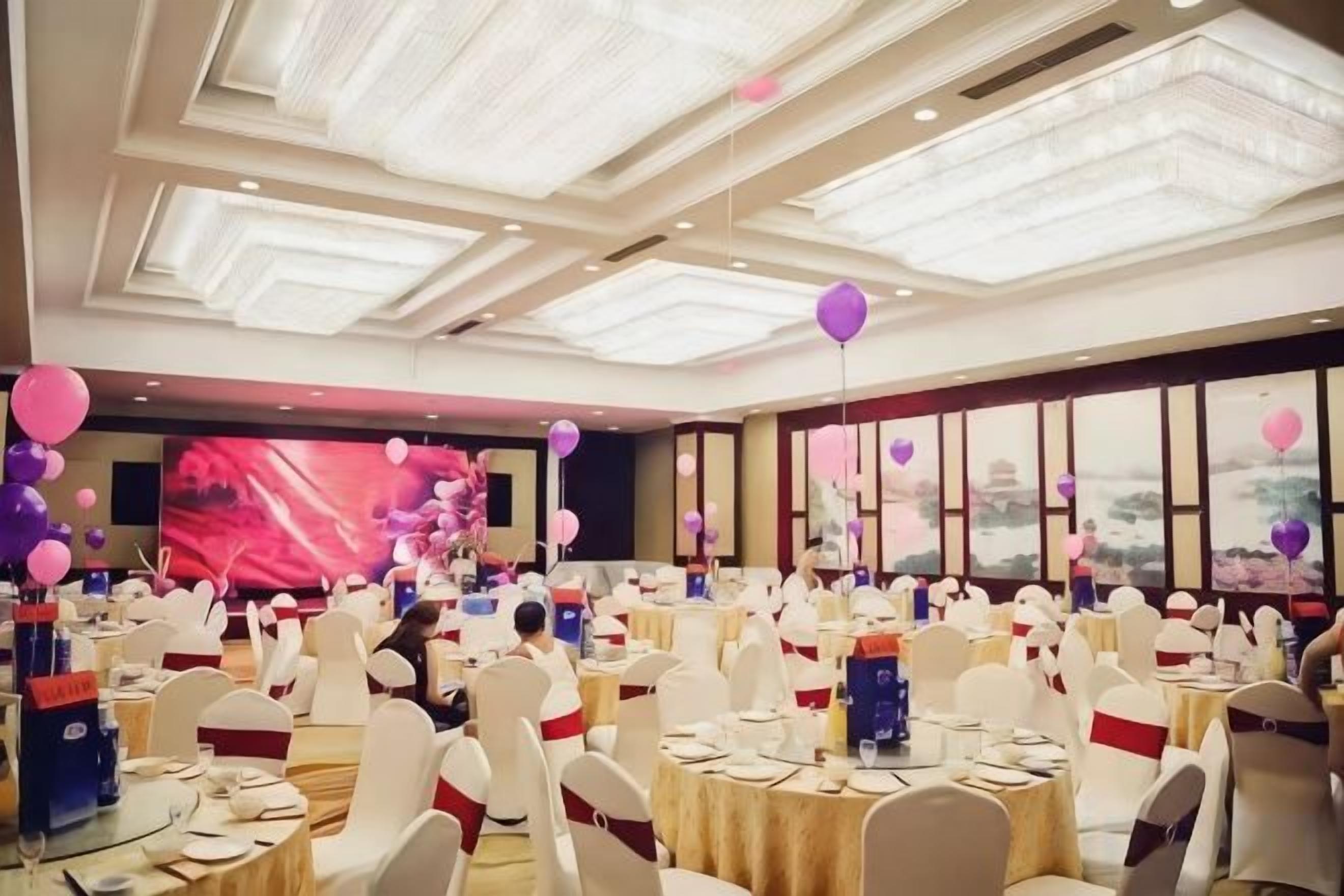 Une salle de banquet avec des tables rondes, des chaises blanches et un grand écran en arrière-plan.