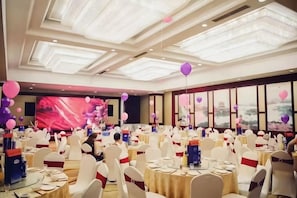 A banquet hall with round tables, white chairs, and a large screen in the background. - Chunlan Business Hotel (Taizhou)