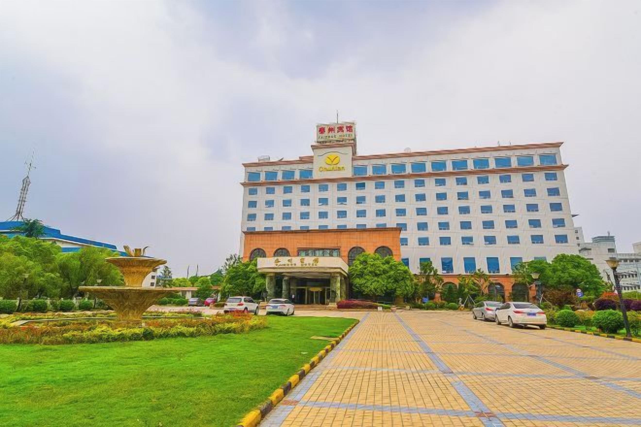 A large hotel with a central entrance, surrounded by a well-maintained garden and a paved driveway.