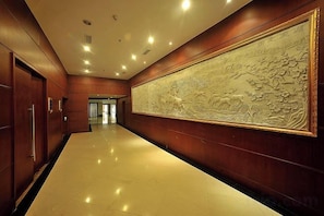 A hallway with a polished floor, wooden paneling, and a large wall-mounted artwork. - Chunlan Business Hotel (Taizhou)