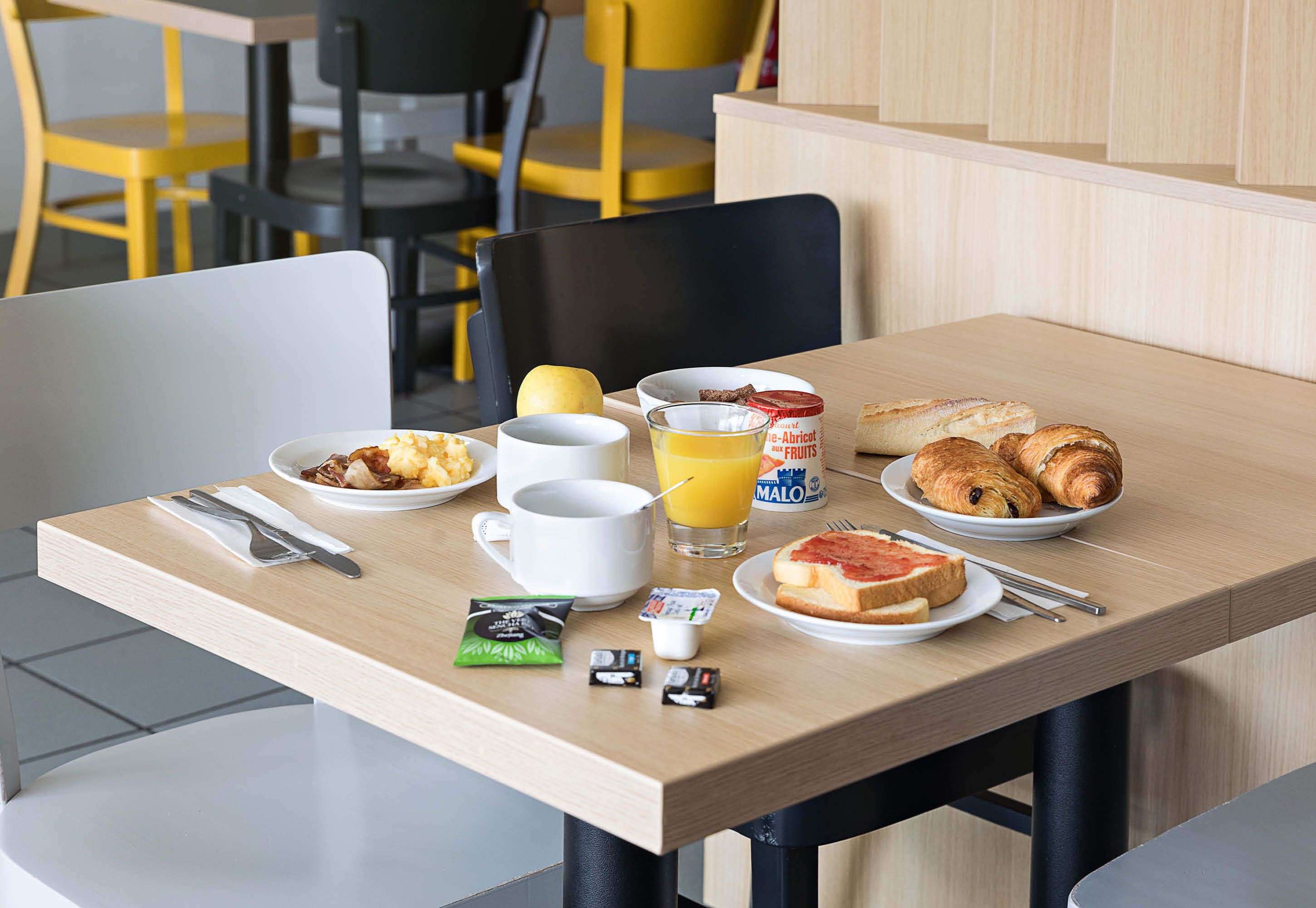 Una mesa de desayuno con tostadas, croissants, un vaso de jugo de naranja, un tazón de cereal y una taza de café.