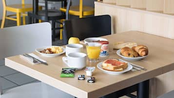 Una mesa de desayuno con tostadas, croissants, un vaso de jugo de naranja, un tazón de cereal y una taza de café.