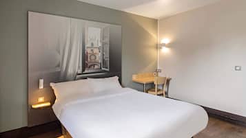 Una habitación de hotel con una cama grande, un escritorio y una silla. Tiene un aplique de pared y una lámpara de mesa.