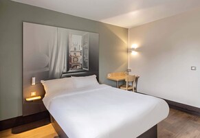 Una habitación de hotel con una cama grande, un escritorio y una silla. Tiene un aplique de pared y una lámpara de mesa.