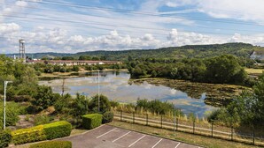 Un parking offrant une vue sur un lac, entouré de verdure et d’un pont situé au loin.