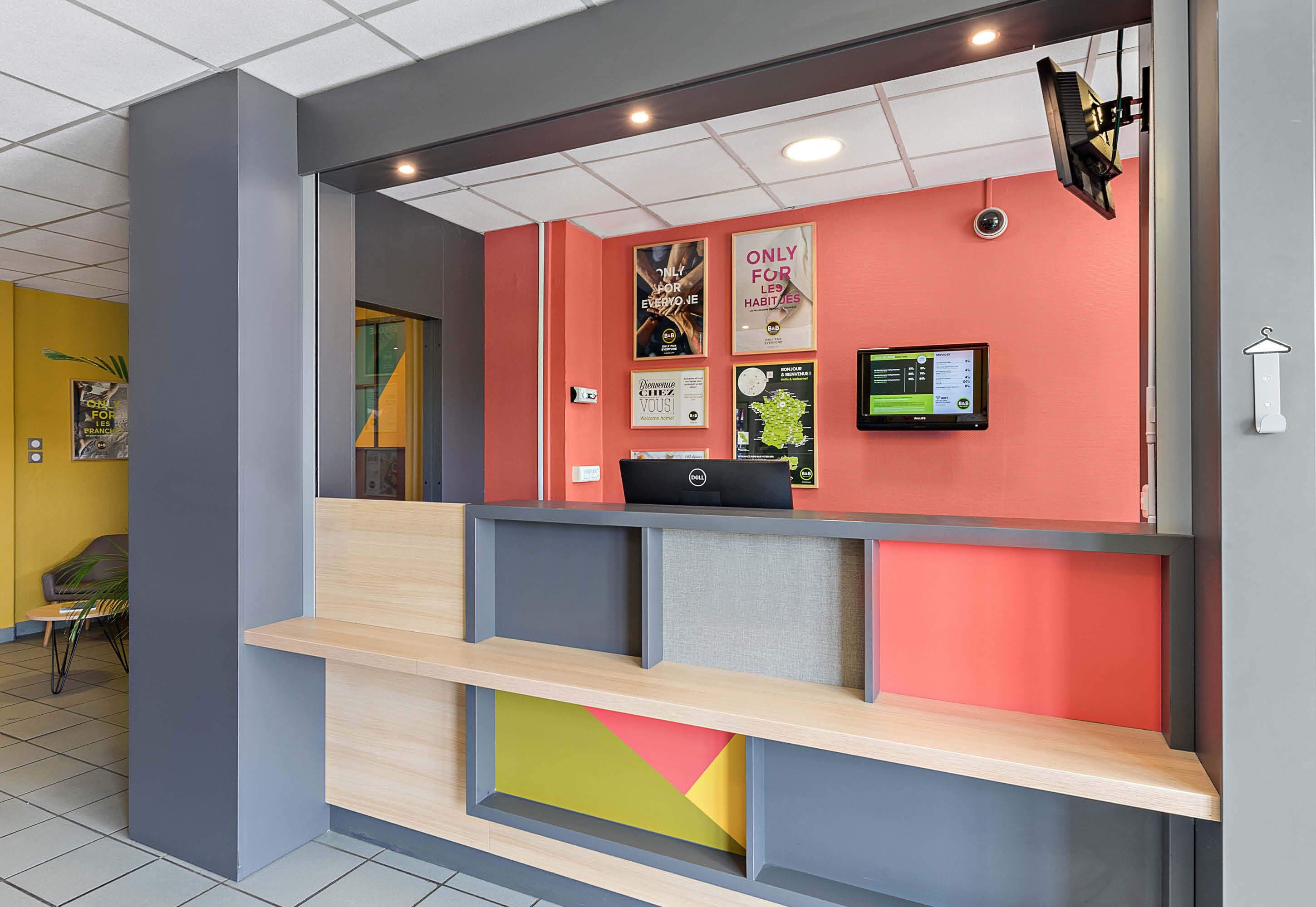 A reception area with a modern design, featuring a counter, a digital screen, and various informational posters on the wall.