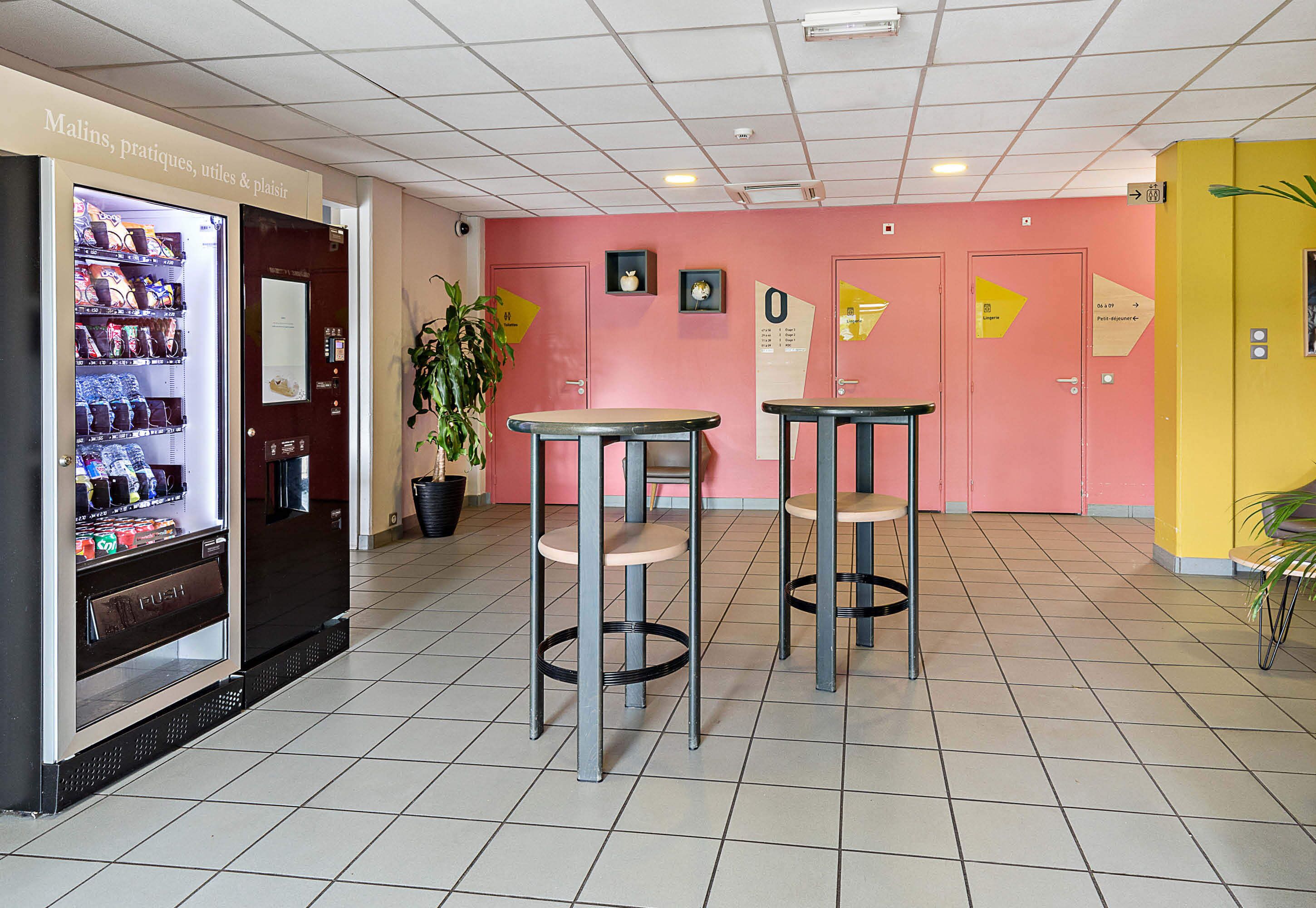A lobby with vending machines, two tables, and a potted plant.