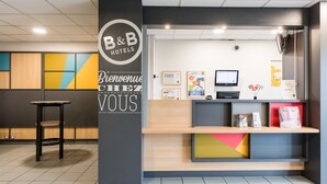 Un comptoir d’accueil avec une enseigne B&B Hotels, un écran d’ordinateur et divers affiches d’information.