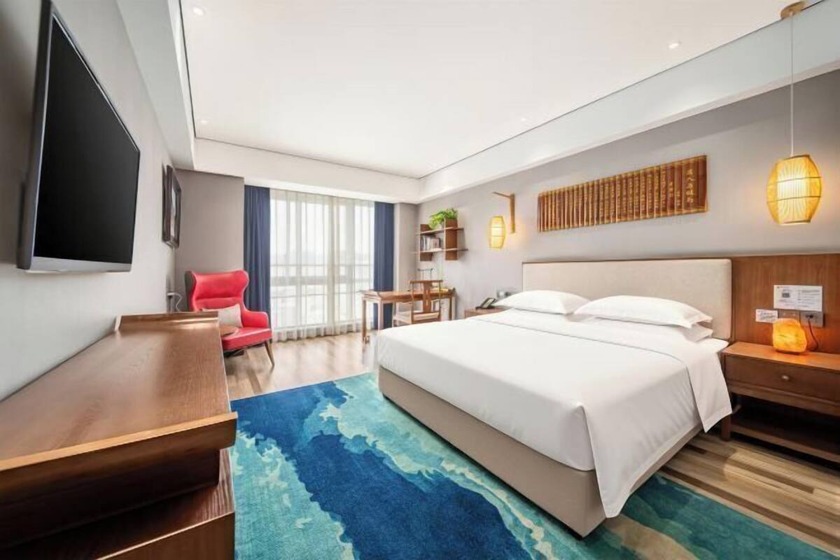 Een moderne hotelkamer met een groot bed, een bureau, een stoel, een televisie en een raam met gordijnen.