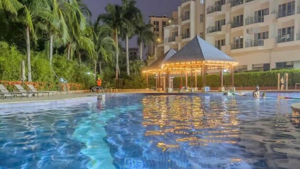 A swimming pool with a gazebo, palm trees, and a building in the background. - Wulan Hot Spring Hotel (Haikou)
