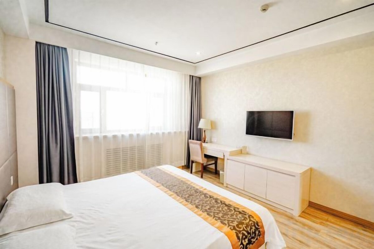 A hotel room with a bed, a desk, a television, and a window with curtains.