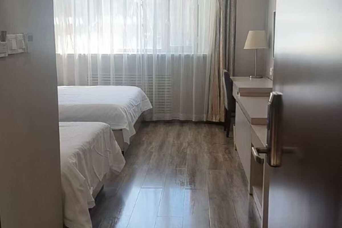 A hotel room with two beds, a desk, a lamp, and a refrigerator.