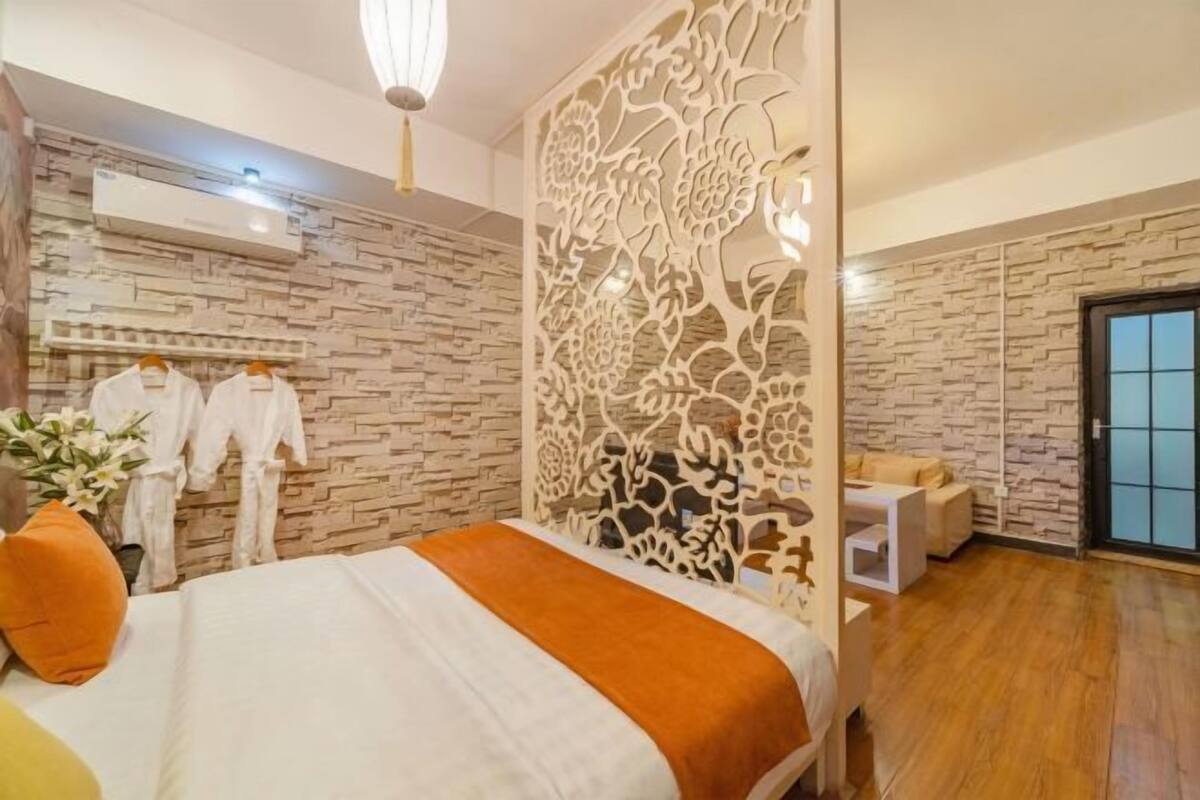 A bedroom with a bed, a decorative partition, a seating area, and a stone-patterned wall.