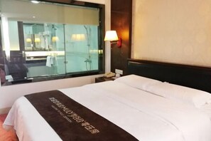 Une chambre d’hôtel avec un grand lit, une table de chevet avec une lampe, une fenêtre donnant sur la salle de bain et un téléphone fixé au mur.