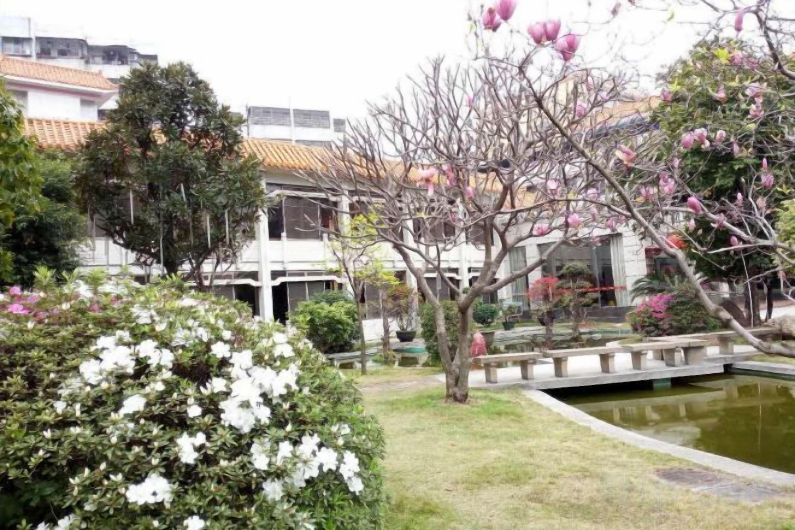 A courtyard with a pond, a bridge, and a building with a tiled roof.