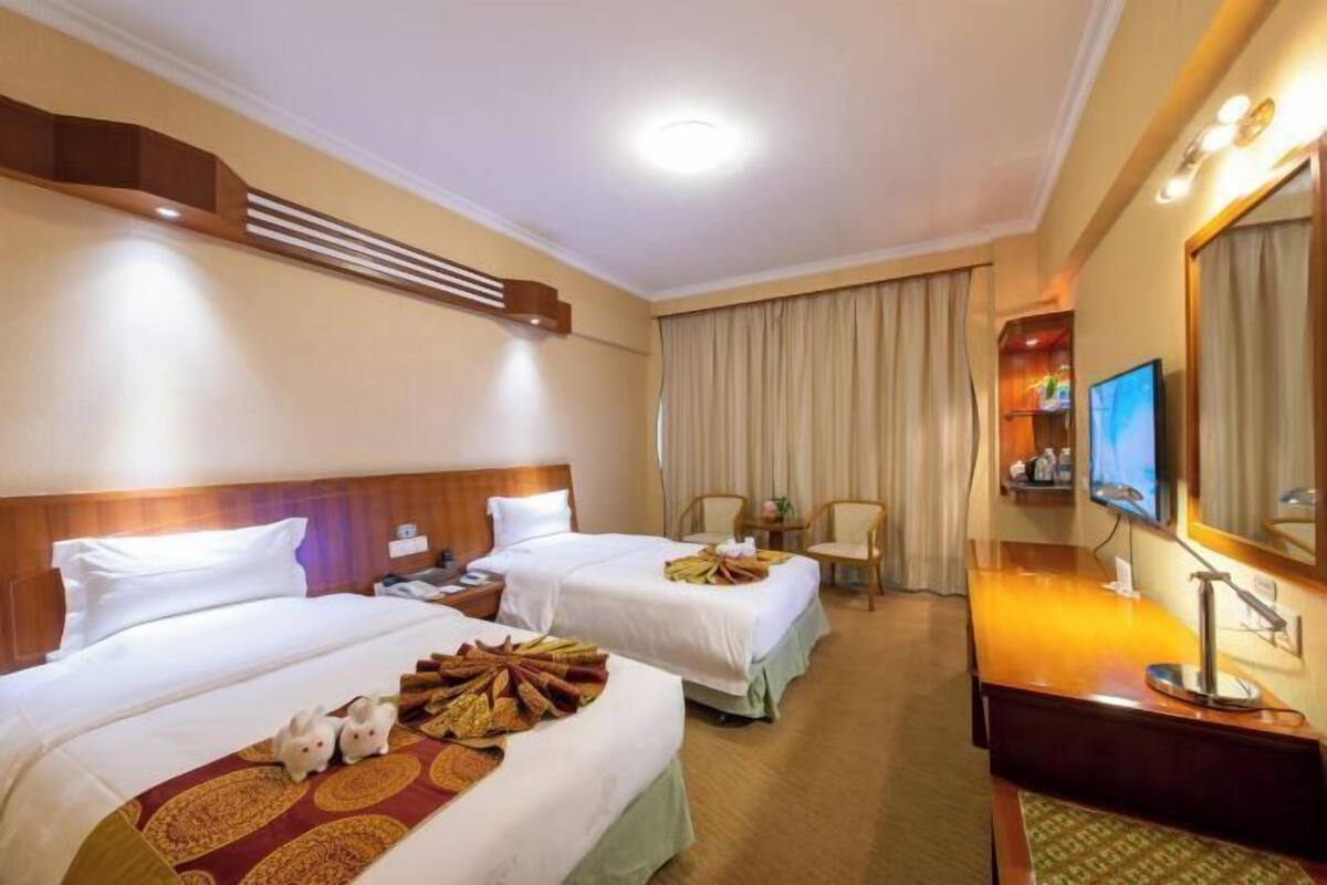 A hotel room with two beds, a television, a desk, and a mirror.