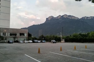 Un estacionamiento con coches y conos de tráfico, un edificio de techo plano, y una montaña al fondo.