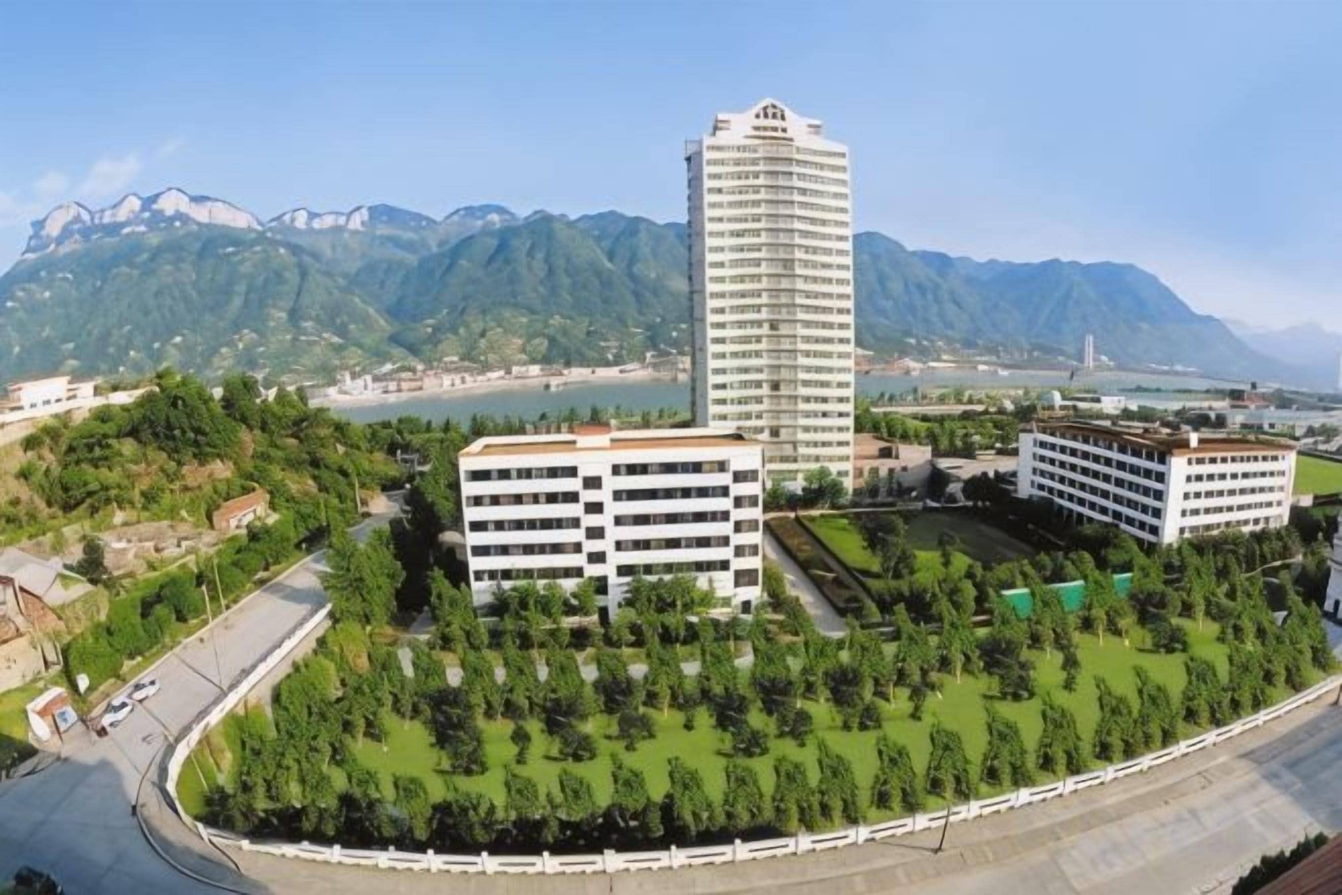 A hotel with a modern design, surrounded by lush greenery and mountains in the background.