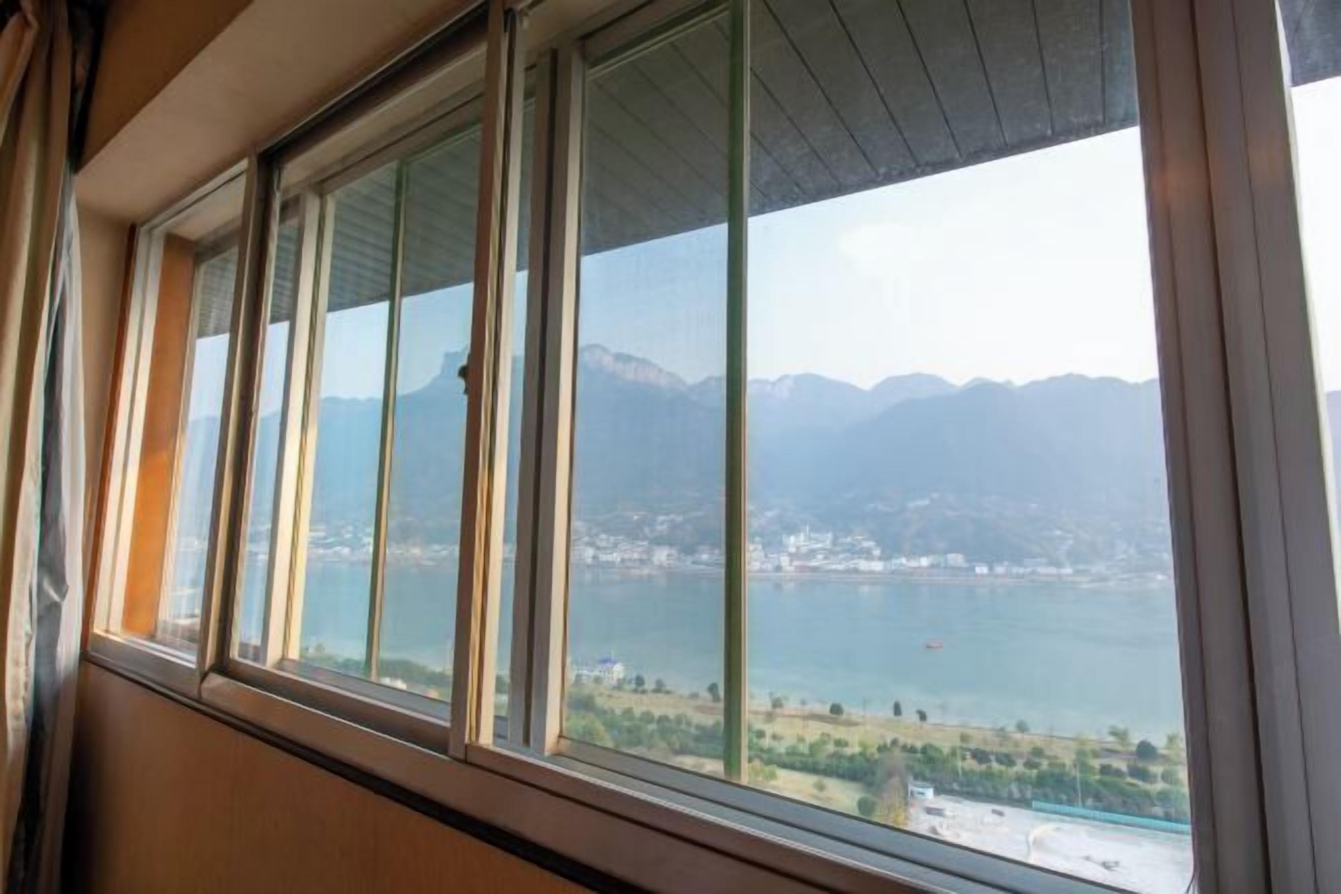 A room with a large window overlooking a lake and mountains.