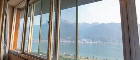 A room with a large window overlooking a lake and mountains.