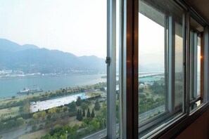A large window with a view of a river, a bridge, and distant mountains.