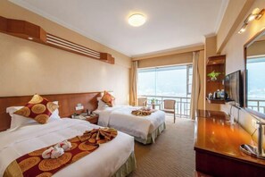 A hotel room with two beds, a TV, a desk, and a balcony with a view.