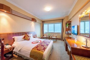 A hotel room with a bed, bedside table, TV, and a view of the city through large windows. - Three Gorges Project Hotel (Yichang)