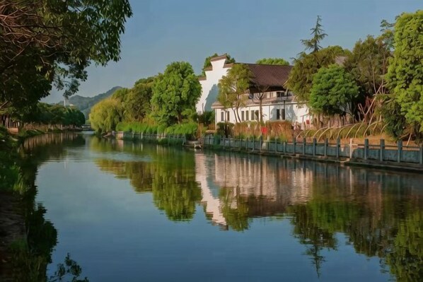 Ein ruhiger Fluss mit einem traditionellen Gebäude am rechten Ufer, umgeben von Bäumen.