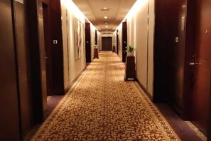 A hotel hallway with carpeted floors, doors on both sides, and a plant in the center. - Qindao International Hotel (Ningbo)
