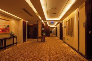 Un pasillo de hotel con piso alfombrado, obras de arte enmarcadas en las paredes y una recepción con una planta.