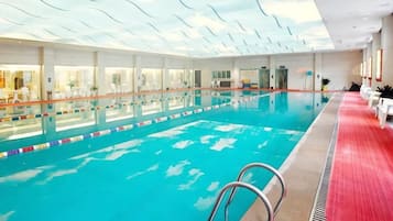 Piscina interna com teto de vidro transparente, assentos à beira da piscina e área com carpete vermelho.