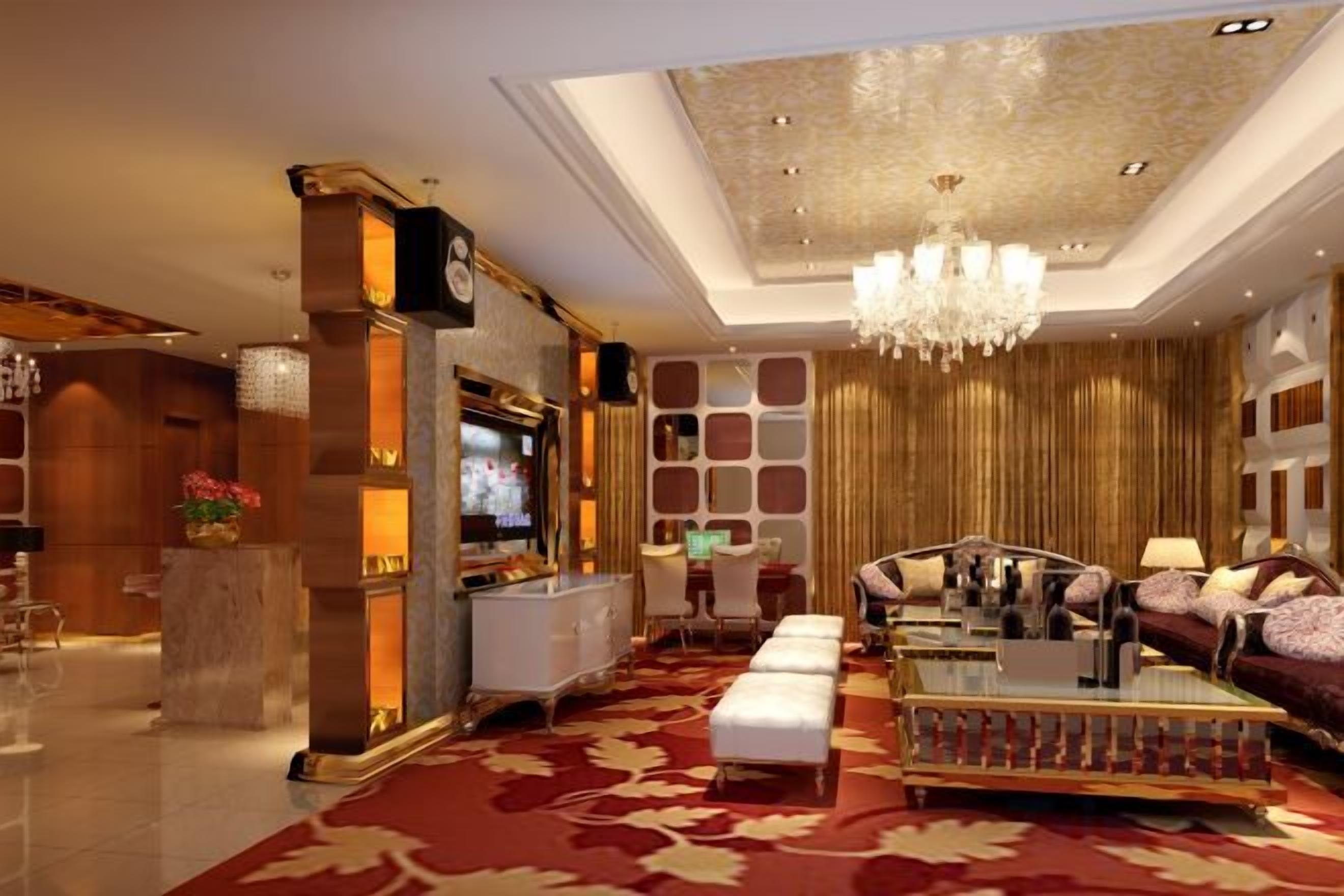 Un amplio vestíbulo con alfombra roja, un candelabro, una zona de estar con sofás y una mesa de centro, y un televisor.