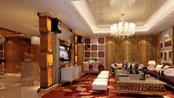 Un amplio vestíbulo con alfombra roja, un candelabro, una zona de estar con sofás y una mesa de centro, y un televisor.