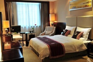 Une chambre d’hôtel avec un lit, un bureau équipé d’un ordinateur, une chaise, une lampe et un tableau au mur.