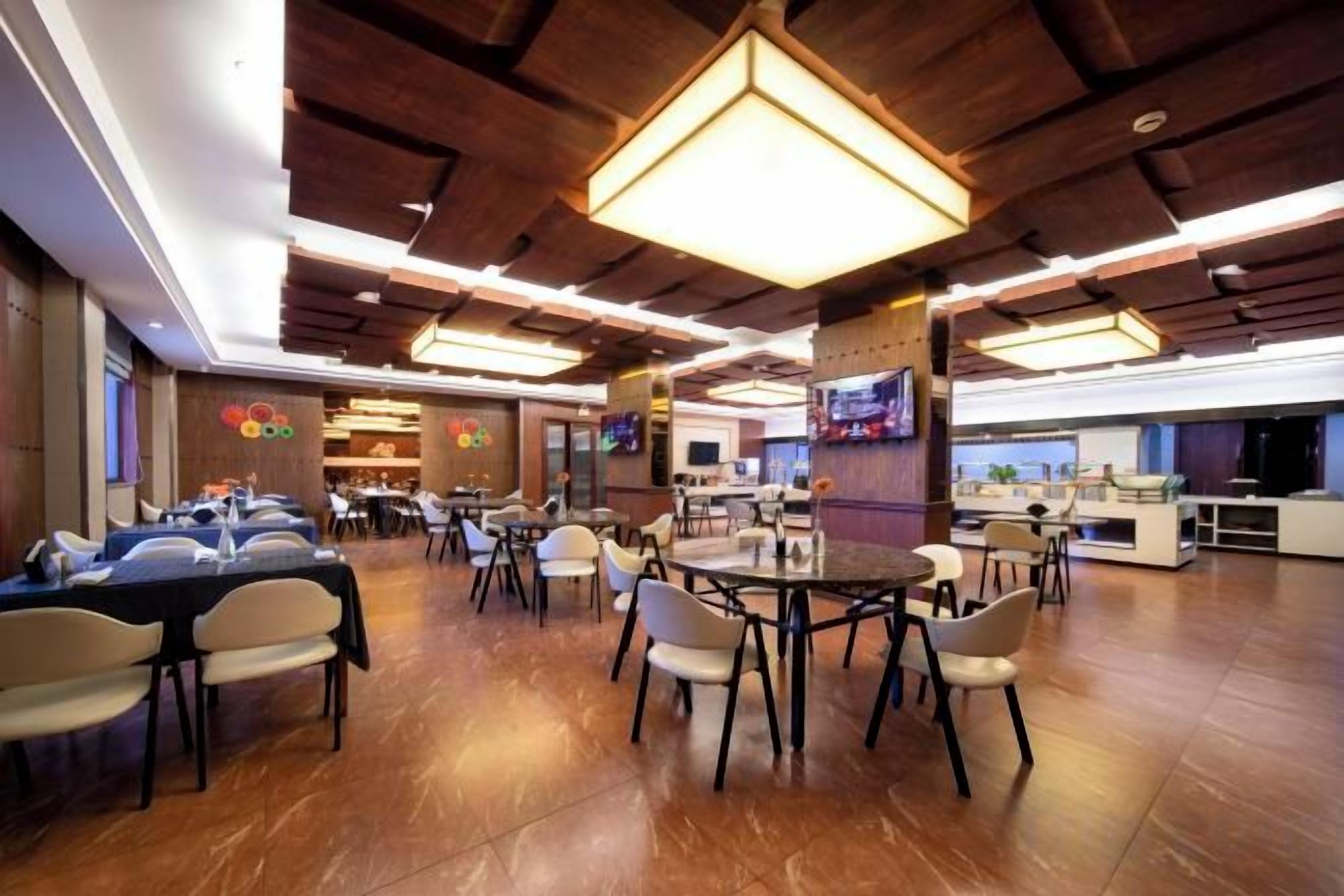 A spacious restaurant with multiple dining tables and chairs, a bar area, and a television screen.