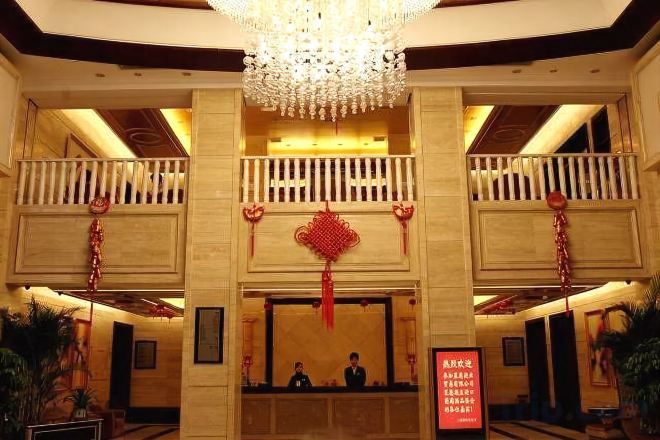 Un vestíbulo de hotel con una imponente lámpara de araña, un mostrador de recepción y un adorno colgante rojo.