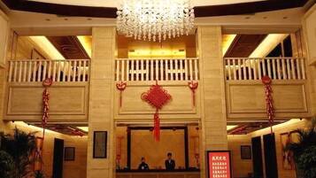 Un vestíbulo de hotel con una imponente lámpara de araña, un mostrador de recepción y un adorno colgante rojo.