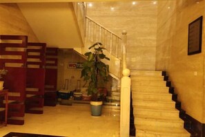 Una escalera con detalles de mármol, una planta en maceta y una silla de madera en un área de recepción.