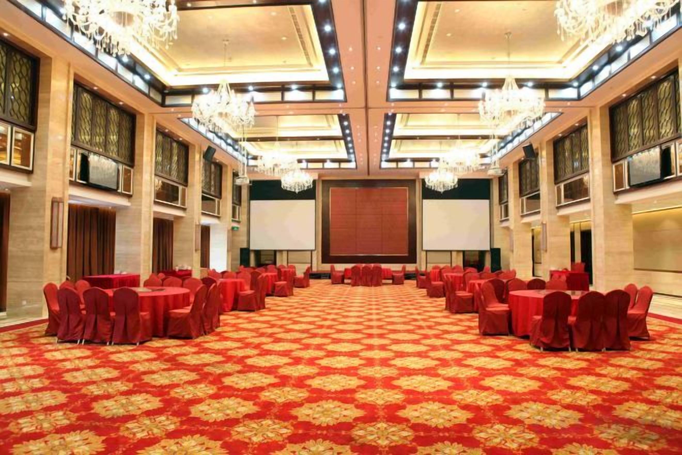 A large conference room with round tables and chairs, a carpeted floor, and chandeliers.