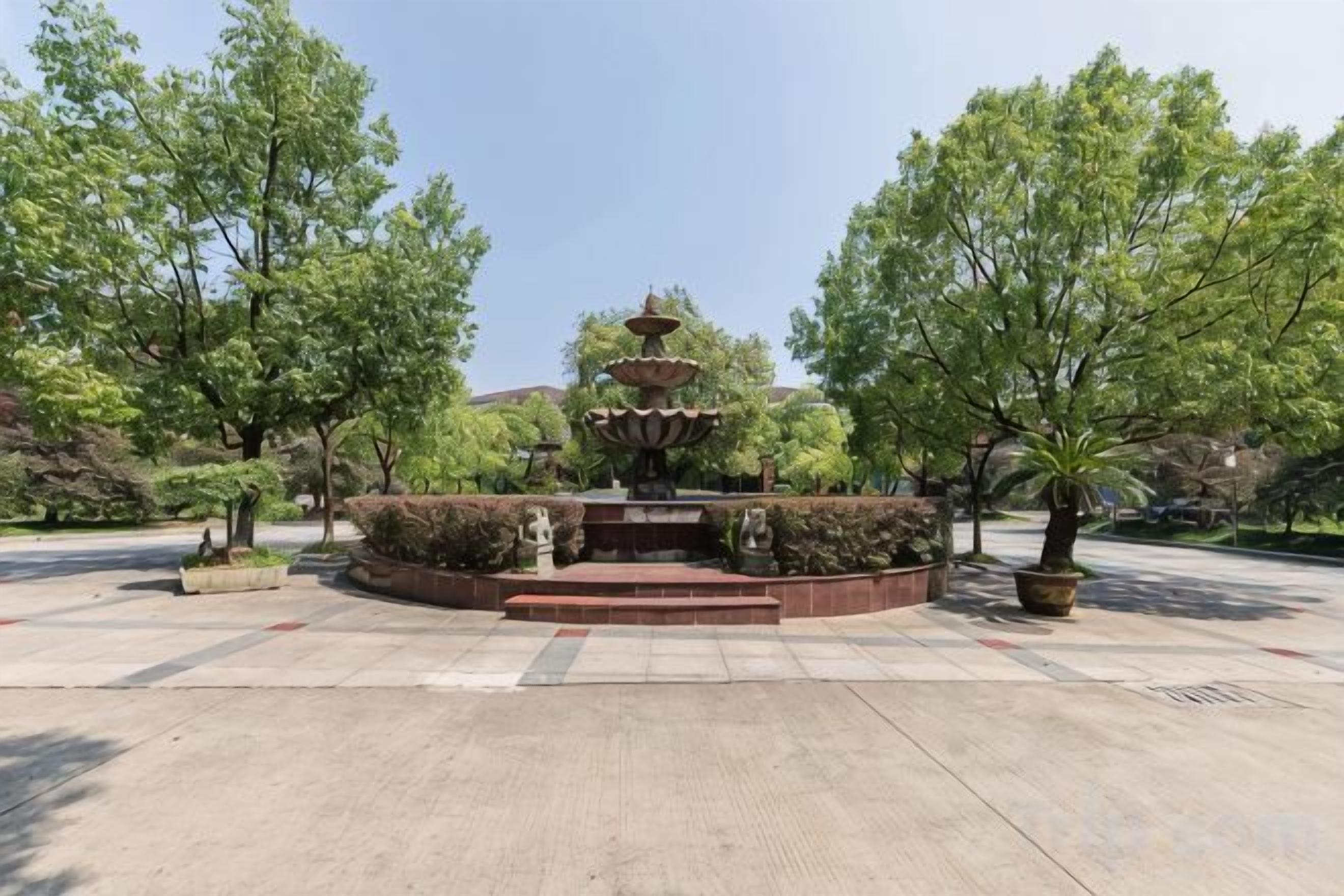 A fountain with multiple tiers in a landscaped area with trees and shrubs.