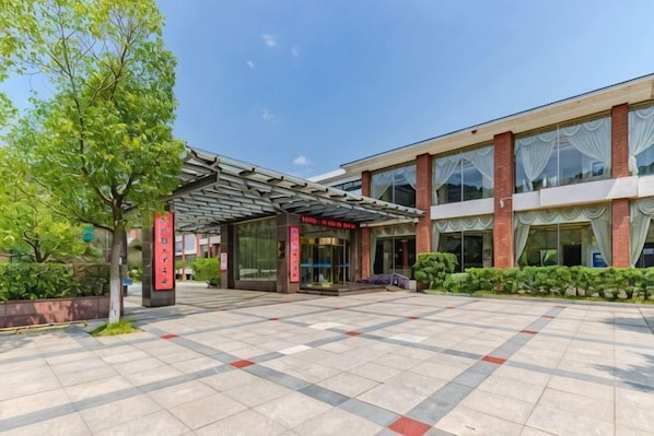 A hotel entrance with a covered walkway, a glass facade, and a tiled courtyard.