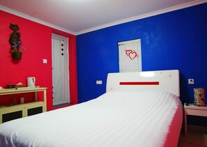 A bedroom with a white bed, a red wall, a blue wall, a white door, a bedside table with a lamp, and a window with a heart design. - Gulangyu Fuxing No.10 Family Inn - Xiamen (Xiamen)