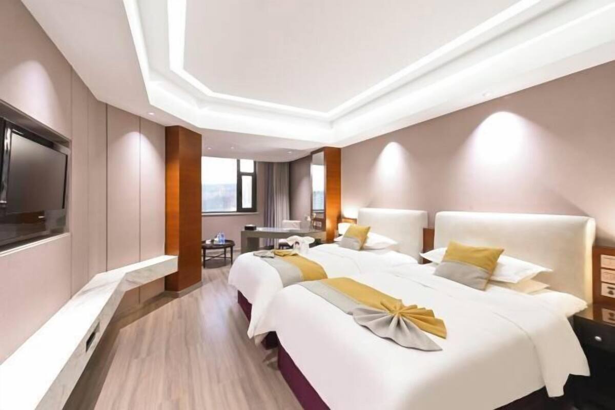 A hotel room with two beds, a desk, a chair, a TV, and a window.