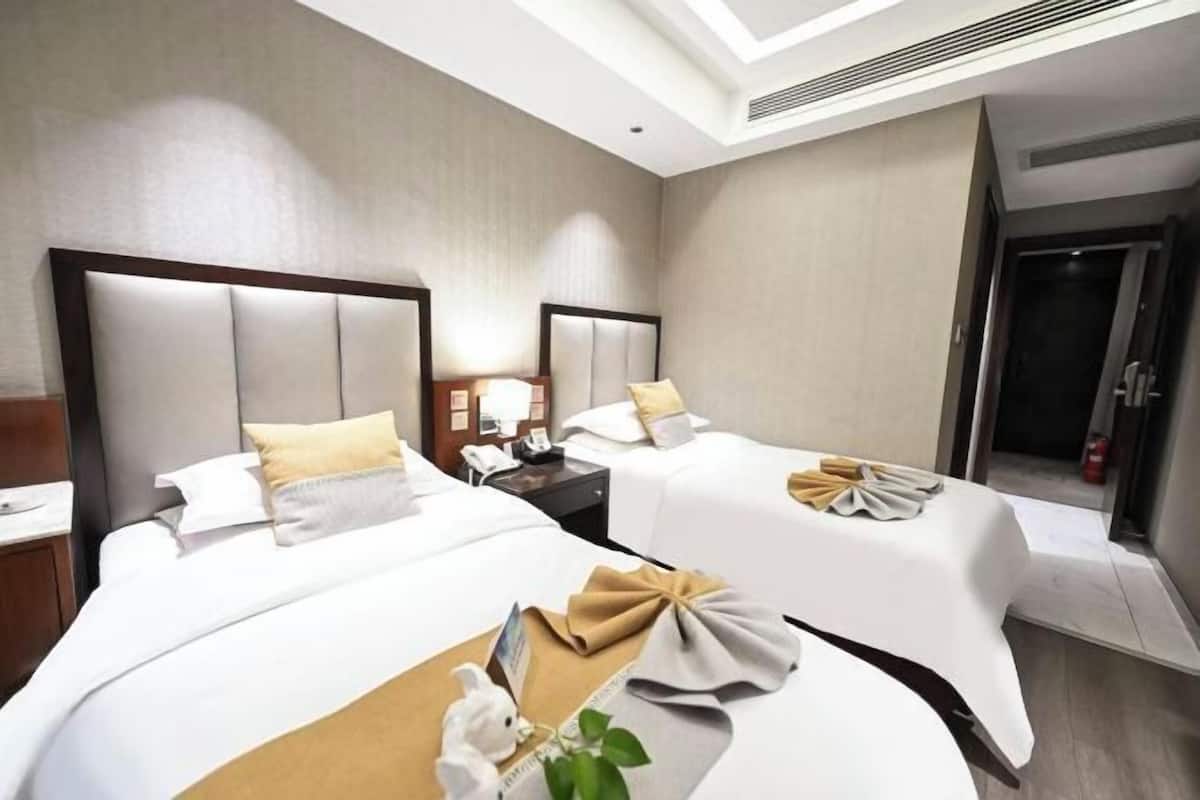A hotel room with two beds, a nightstand, a lamp, and a mirror.