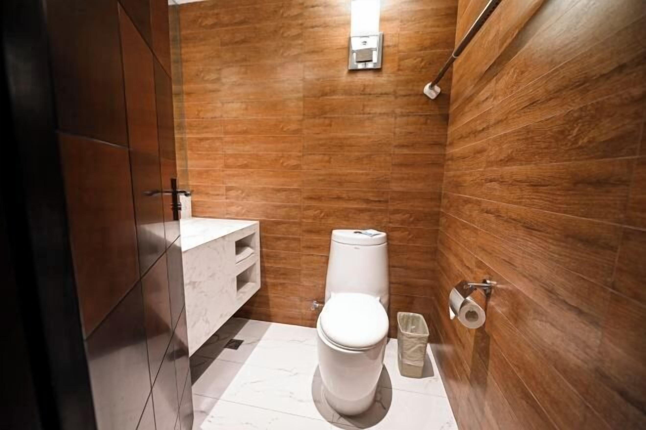 A modern bathroom with a wooden wall, a white toilet, a marble sink, and a towel rack.