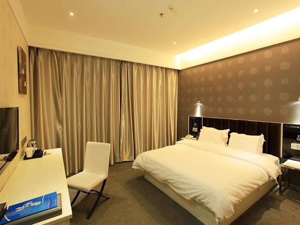 Een hotelkamer met een groot bed, een bureau, een stoel, een televisie en gordijnen.