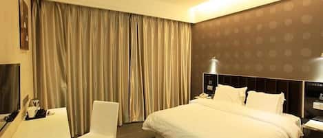 Een hotelkamer met een groot bed, een bureau, een stoel, een televisie en gordijnen.