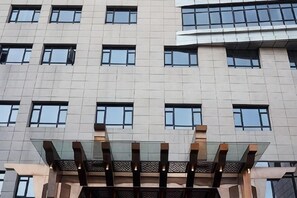 Un edificio de varios pisos con un diseño arquitectónico moderno, que presenta una serie de ventanas rectangulares y una estructura de vidrio a nivel de calle.
