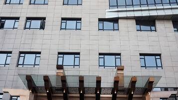 Un edificio de varios pisos con un diseño arquitectónico moderno, que cuenta con una serie de ventanas rectangulares y una estructura de vidrio en la entrada.