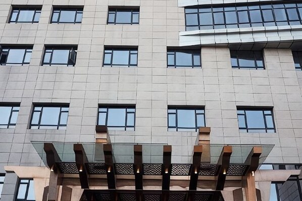 A multi-story building with a modern architectural design, featuring a series of rectangular windows and a glass structure at the entrance. - Haina Baichuan Hotel (Ningbo)